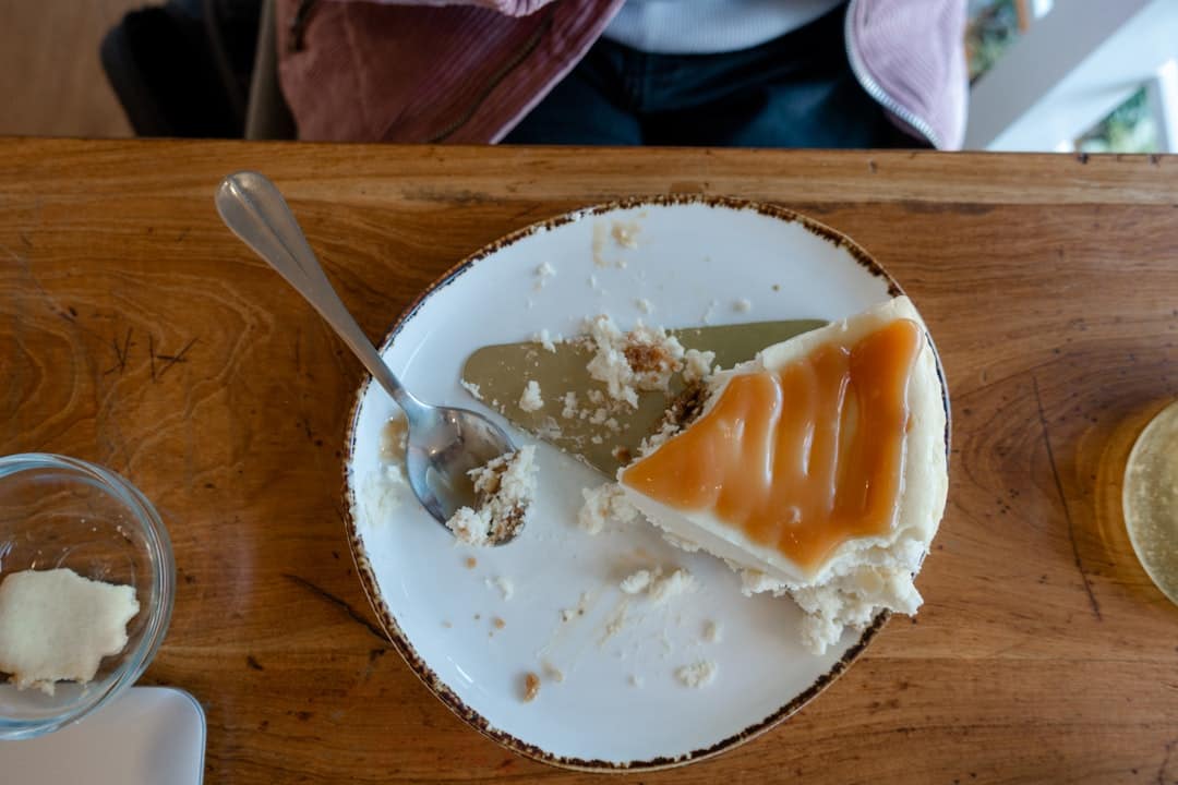 Um Prato Branco Coberto Com Um Pedaco De Bolo Ao Lado De Uma Colher NT_sUGIPH5I