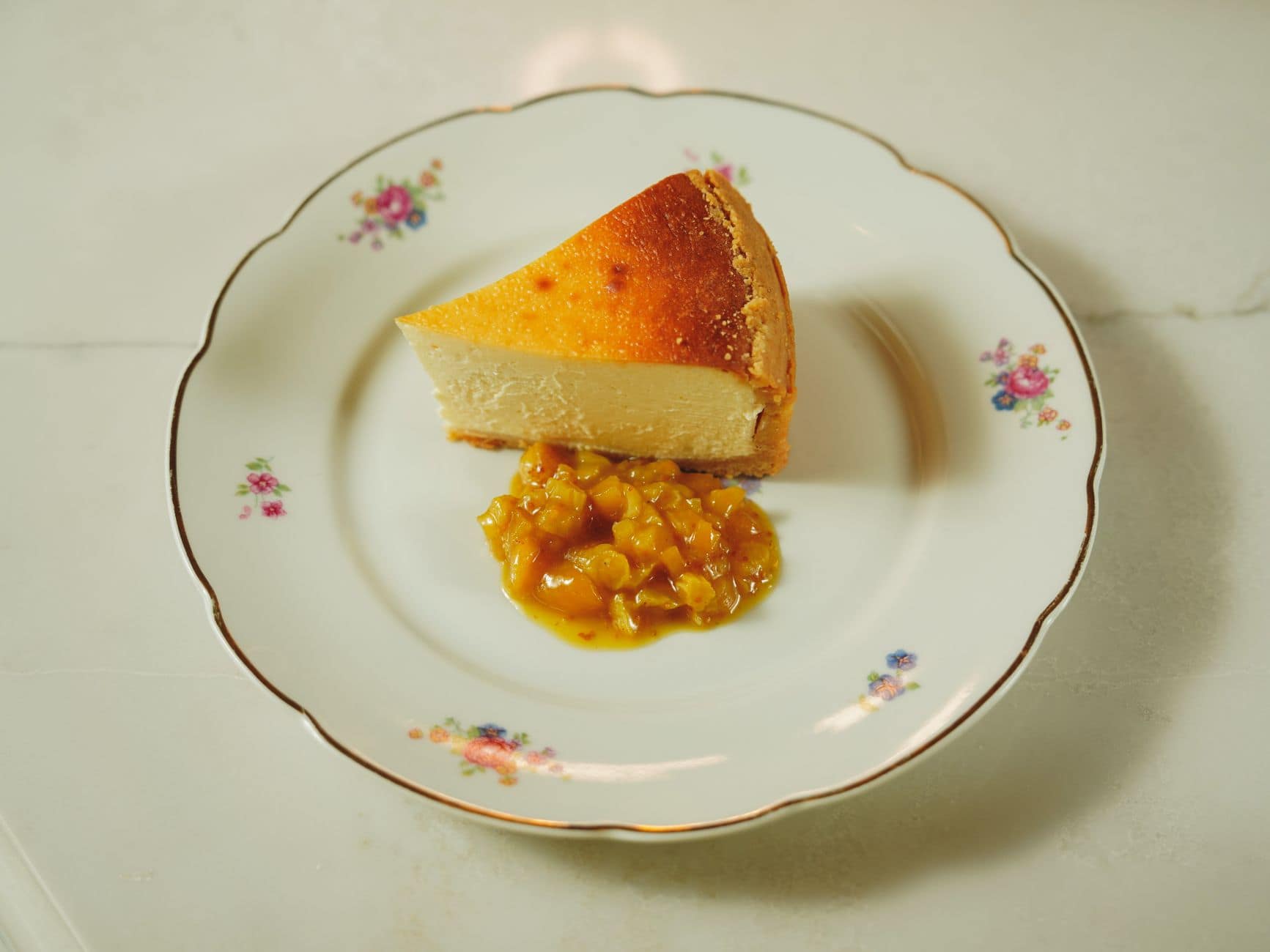 Elegant slice of cheesecake on a decorative floral plate with fruit topping.