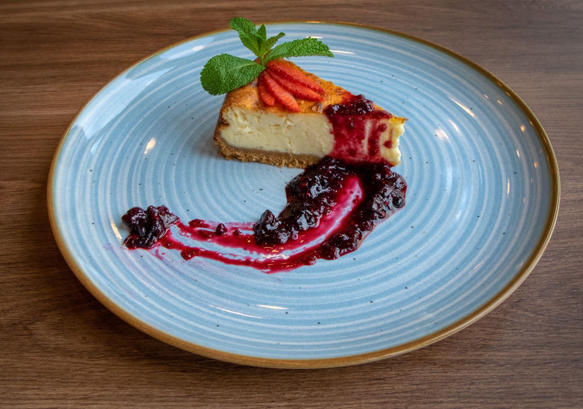 Close-up of a cheesecake slice with fruit garnish on a blue plate, perfect for dessert lovers.