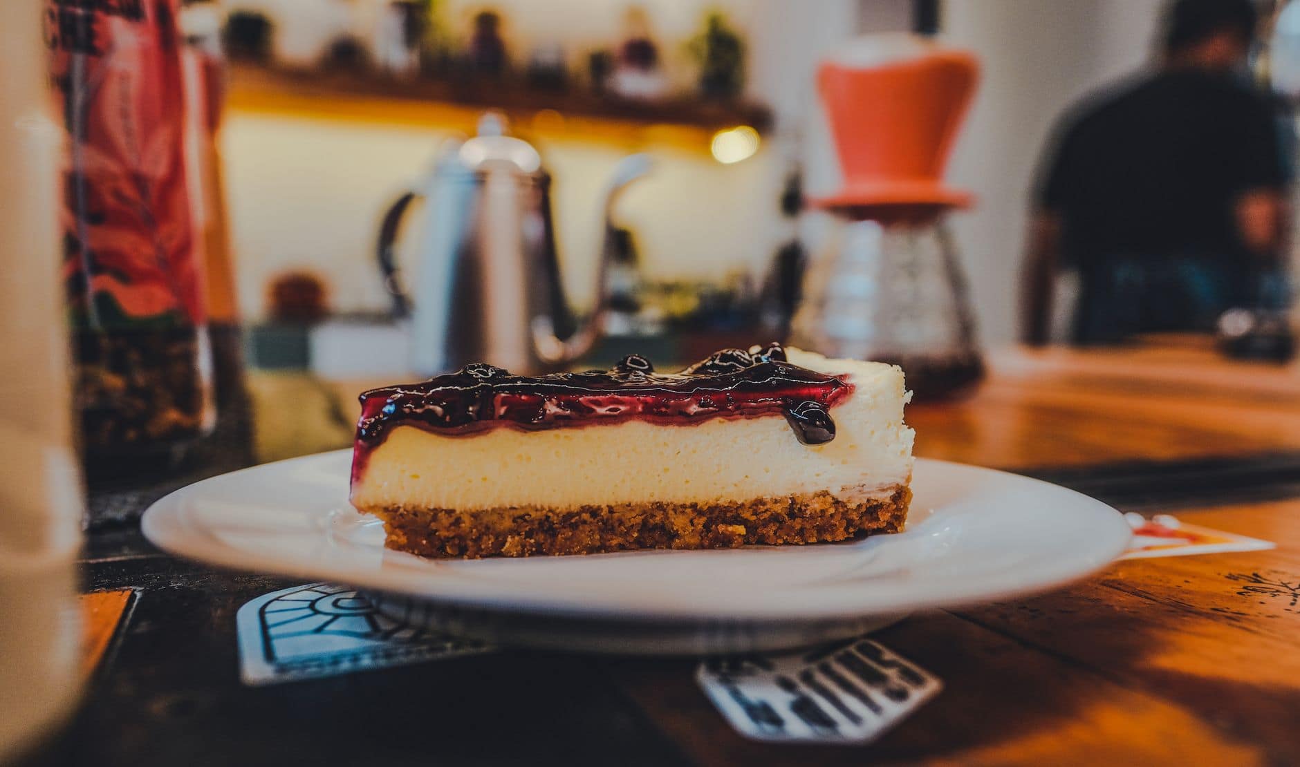 Mouthwatering slice of blueberry-topped cheesecake on a plate in a cozy cafe setting.