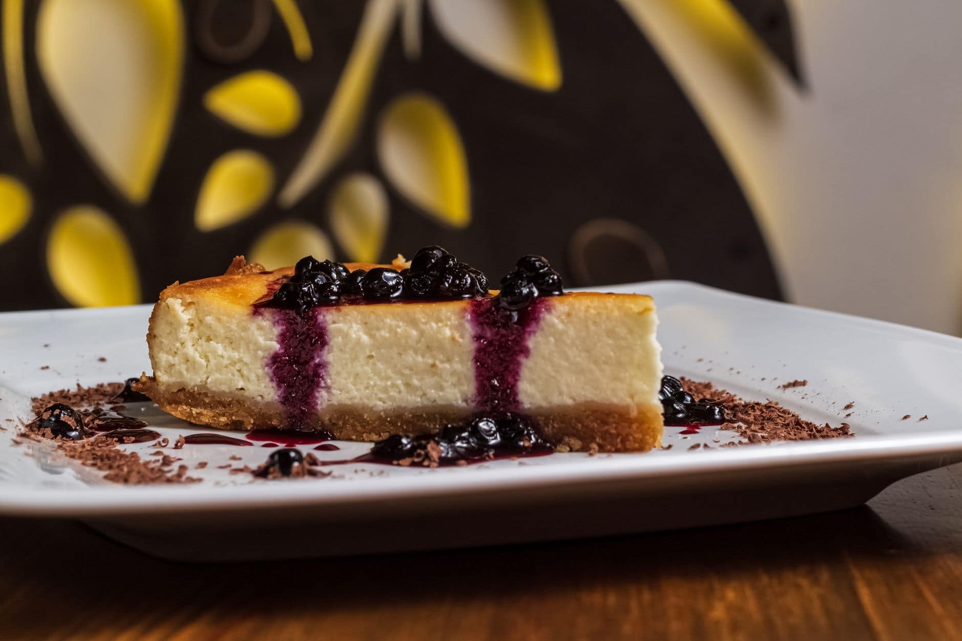 Close-up of a creamy cheesecake slice topped with blueberries and chocolate shavings.