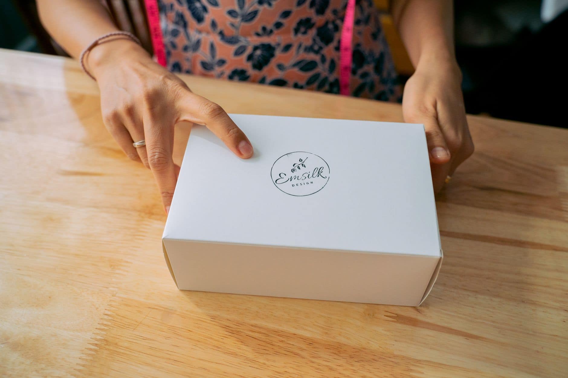 Close-up of hands holding a white branded box on a wooden table.