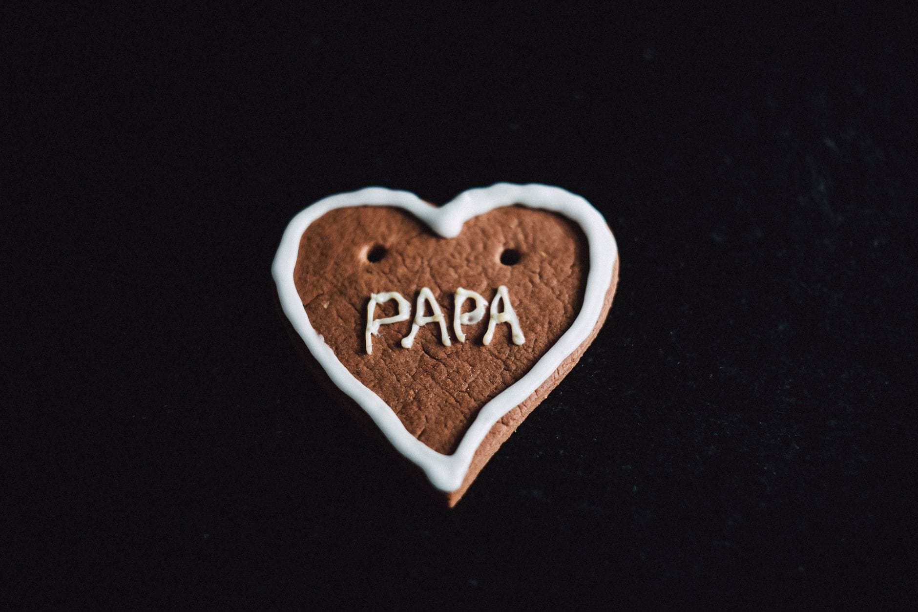 A heart-shaped gingerbread cookie with 'Papa' icing on a black background, perfect for Father's Day.