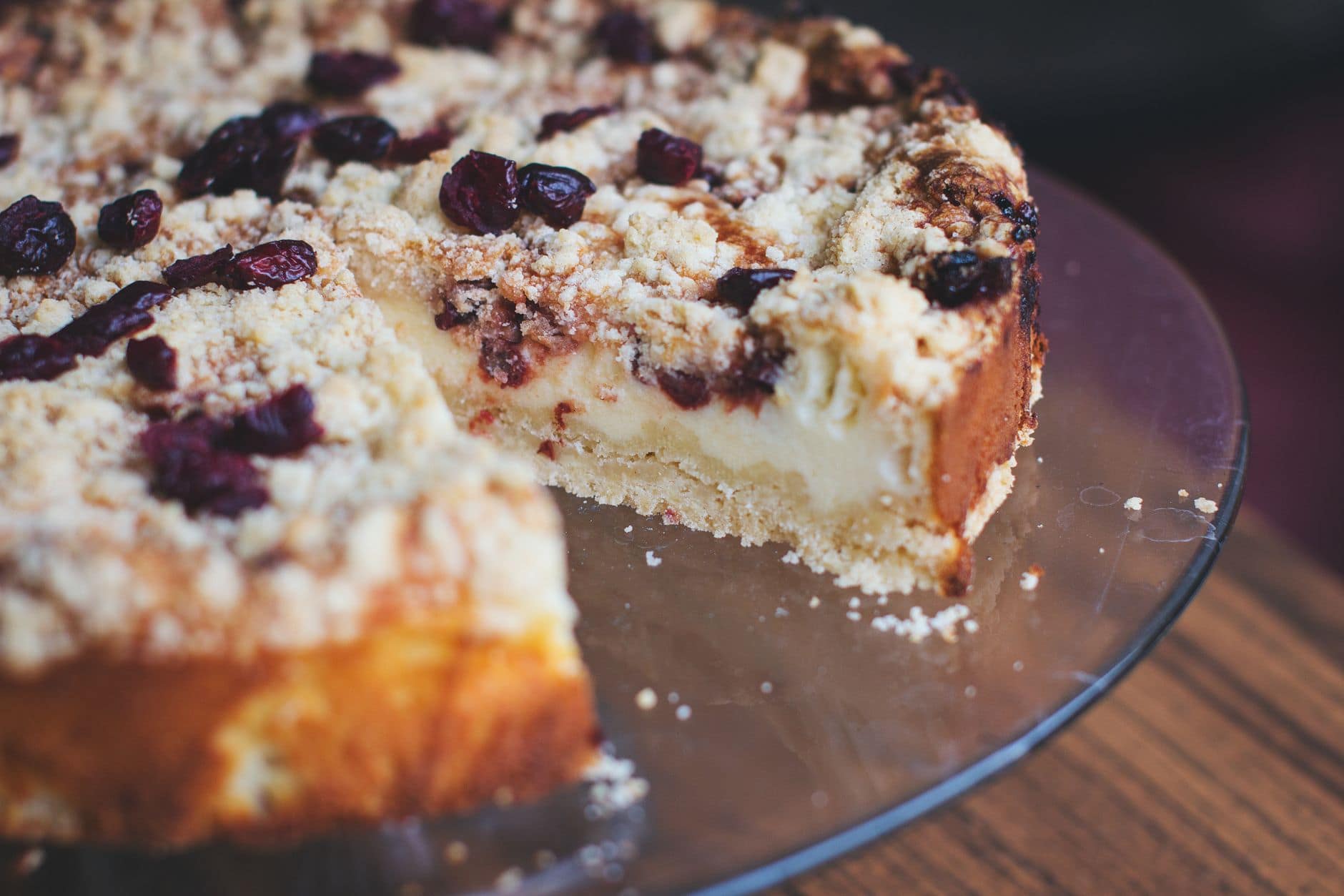 A close-up image of a slice of cherry cheesecake with a streusel topping on a glass plate.