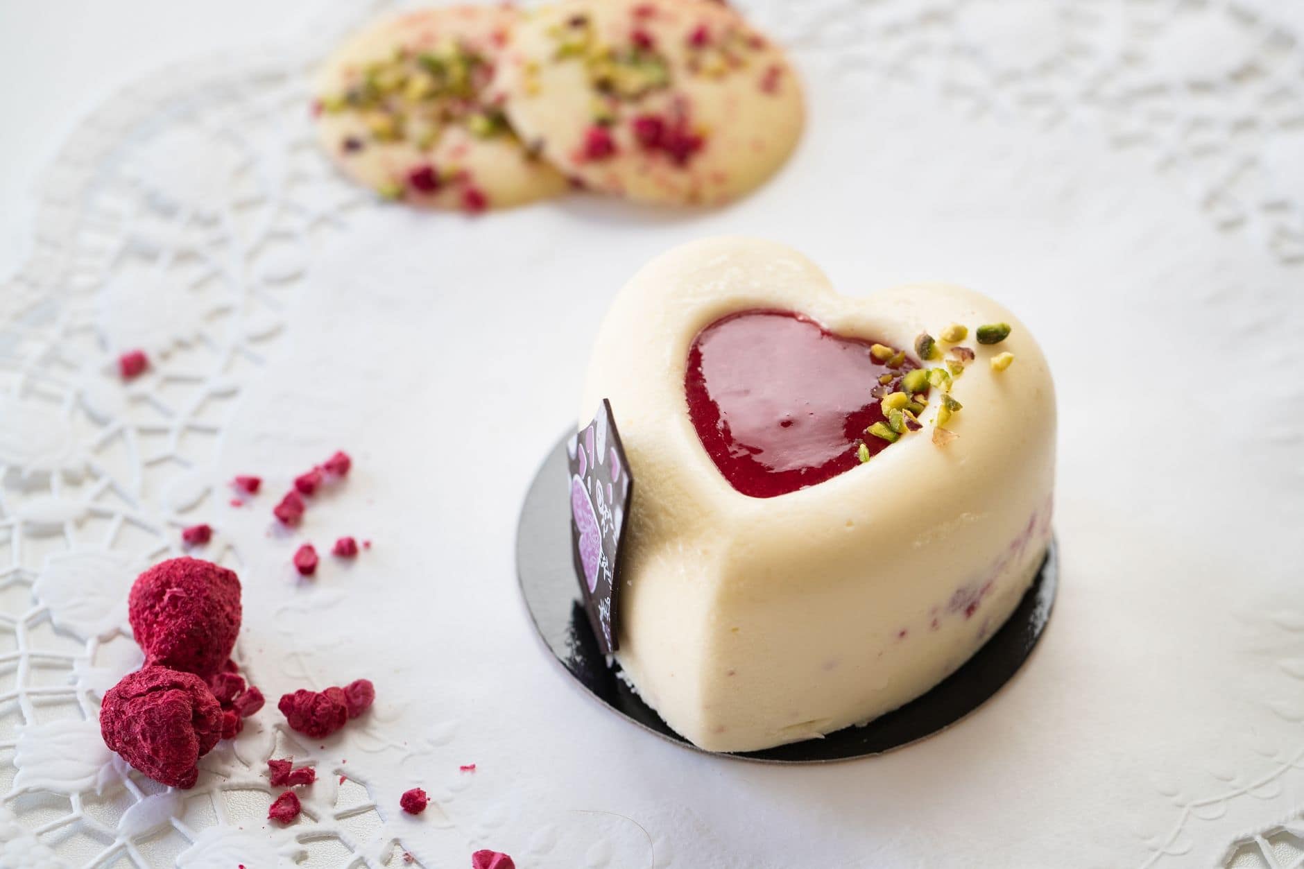 A delicious heart-shaped cake with raspberry center and pistachio garnish, set on a lace background.