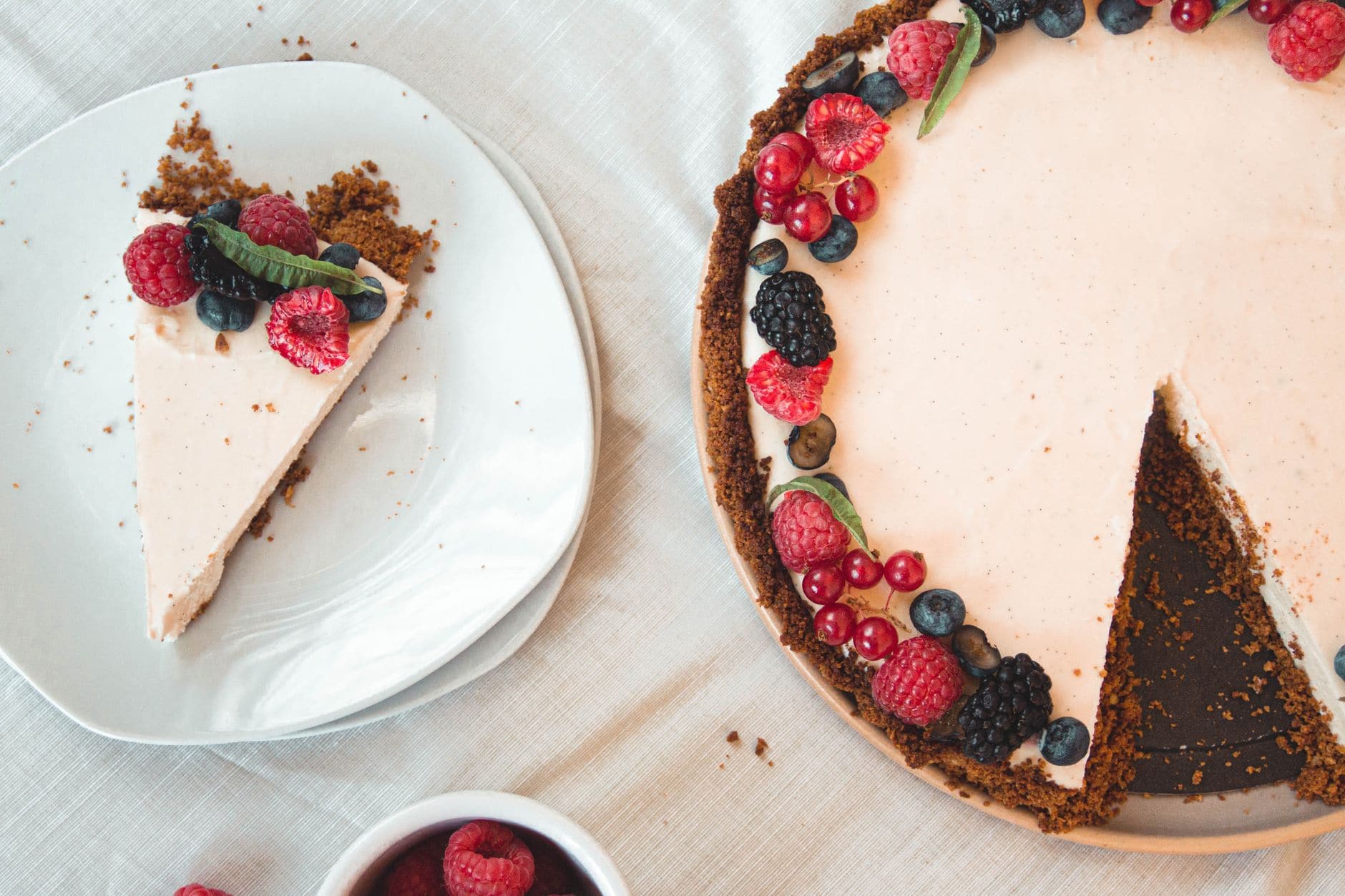 Top view of a berry-decorated cheesecake with a slice on a white plate.