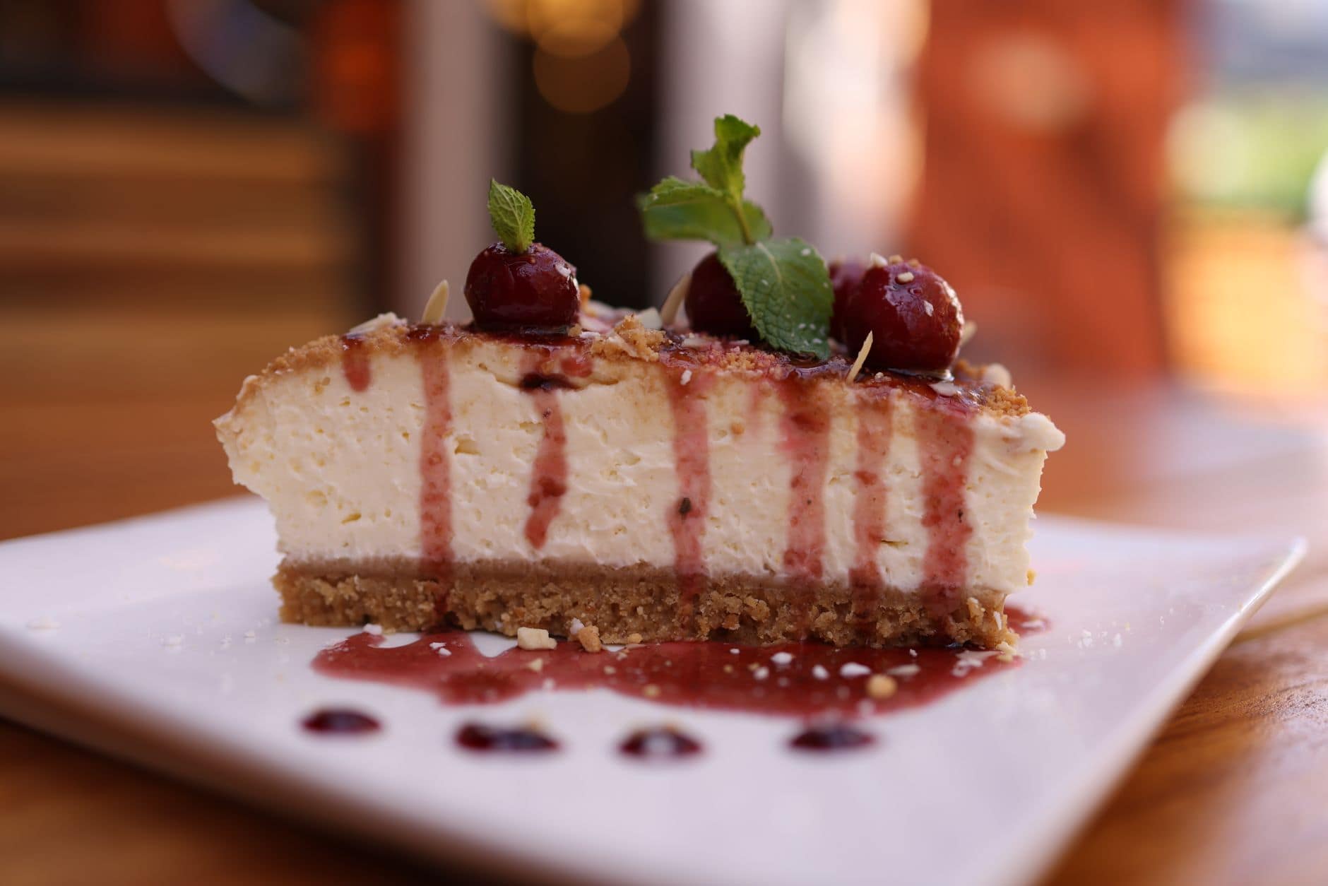 Close-up of a creamy cheesecake slice with cherry topping and mint garnish.