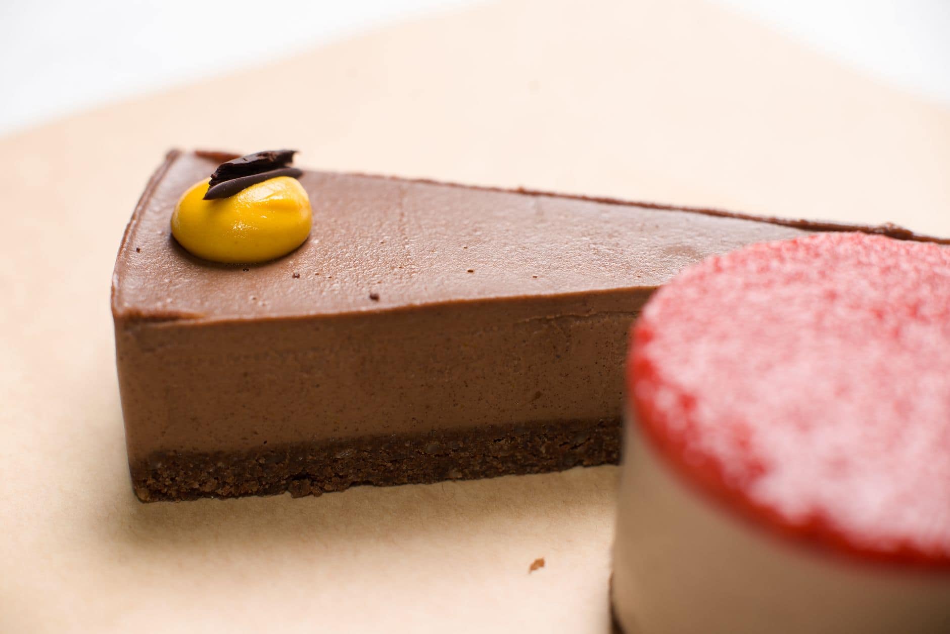 Close-up of a chocolate dessert slice with mango glaze on parchment paper.