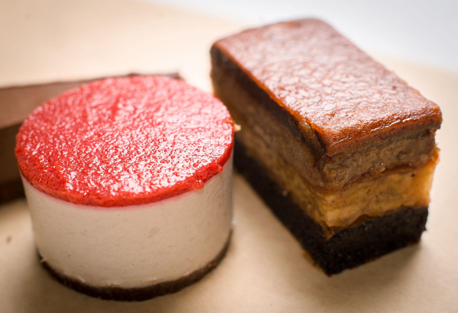 A close-up of a gourmet cheesecake with a strawberry topping next to a layered chocolate dessert.